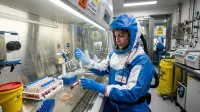 Scientifique en combinaison de protection manipulant des échantillons dans un laboratoire de haute sécurité.