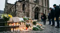 Bougies et fleurs devant un lieu de culte endommagé, hommage aux victimes de violences religieuses.