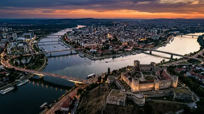Vue aérienne de Belgrade au crépuscule, avec la forteresse de Kalemegdan dominant la confluence de la Save et du Danube, symbole des tensions géopolitiques entre Est et Ouest.
