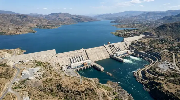 Vue aérienne du grand barrage éthiopien de la Renaissance sur le Nil Bleu, son réservoir en eau et ses turbines, sous un ciel dégagé.