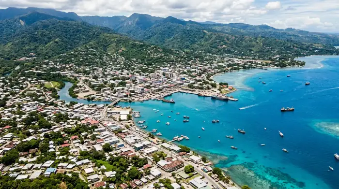 Vue aérienne de Honiara, capitale des Îles Salomon, avec le lagon bleu et les collines verdoyantes en arrière-plan.