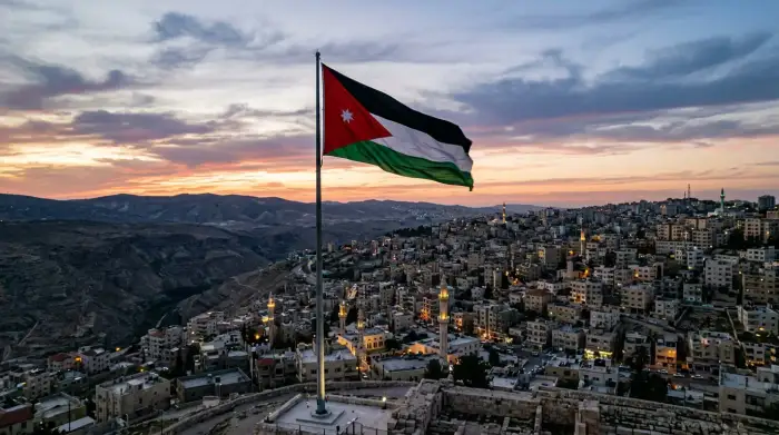 Drapeau jordanien flottant au-dessus d'Amman au crépuscule, regard tourné vers l'ouest, la vallée du Jourdain et les collines de Cisjordanie.