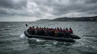 Une barque de migrants traverse la Manche au large des côtes anglaises, sous un ciel gris.